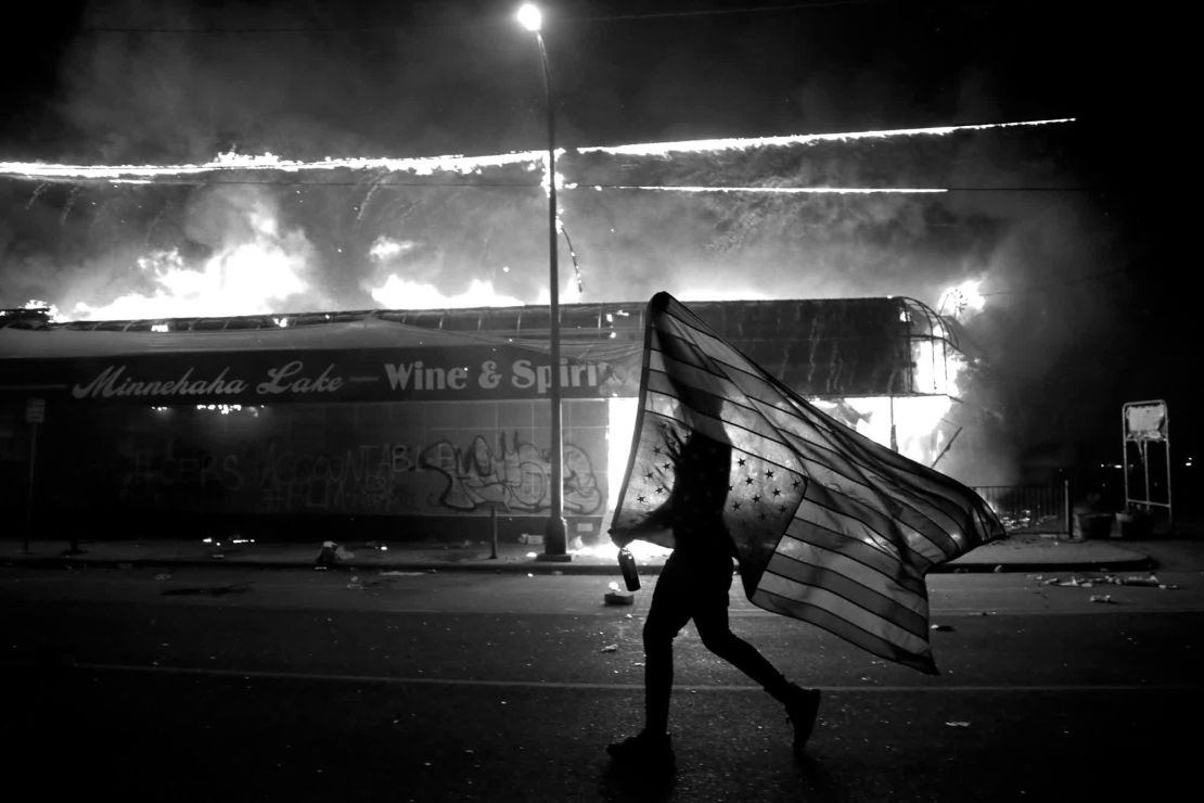 Un manifestante lleva una bandera estadounidense al revés junto a un edificio en llamas en Minneapolis el año pasado. Crédito: Julio Cortez / AP