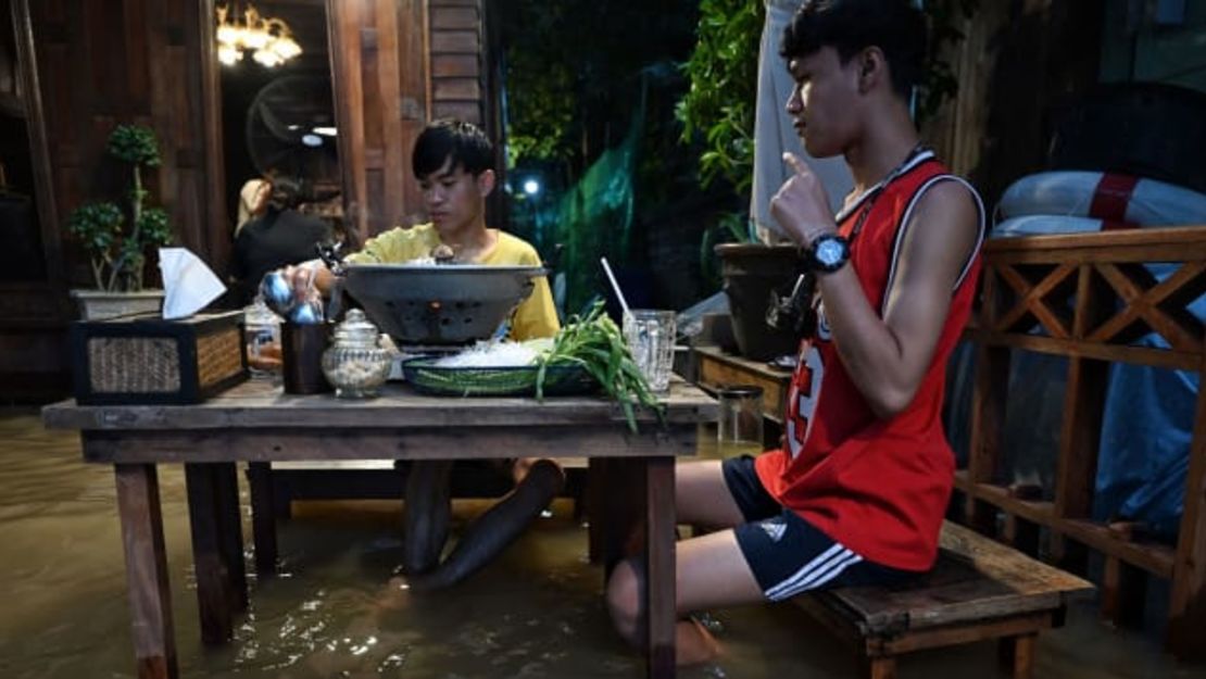 La gente disfruta de sus alimentos en el Chaopraya Antique Cafe, mientras el agua de la crecida del río Chao Phraya entra en el restaurante. Créditos: Lillian Suwanrumpha/AFP/Getty Images