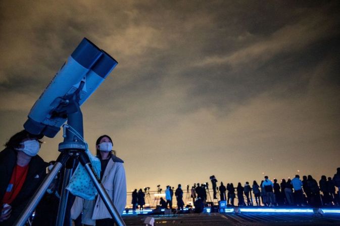 Personas observan el cielo nocturno con un telescopio mientras fotógrafos y reporteros gráficos documentan un eclipse lunar desde la plataforma de observación de Roppongi Hills en Tokio.