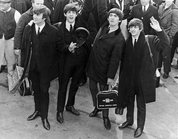 Alrededor de 1964: The Beatles saludan a una multitud en un aeropuerto a su llegada a Estados Unidos para dar conciertos y aparecer en televisión.