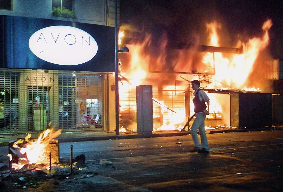 Un agente de policía, vestido de civil y armado, avanza frente a un comercio incendiado en la noche del 20 de diciembre de 2001.