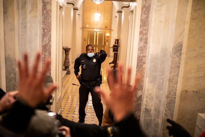 6 de enero — el policía del Capitolio de Estados Unidos, Eugene Goodman, se enfrenta a los manifestantes mientras asaltan el edificio. Cinco personas murieron como resultado de los disturbios, incluida una mujer a la que la policía disparó fatalmente y tres personas que murieron por aparentes emergencias médicas. Entre los que murieron se encontraba el agente Brian Sicknick, quien sufrió derrames cerebrales y murió de causas naturales un día después de responder a la insurrección.