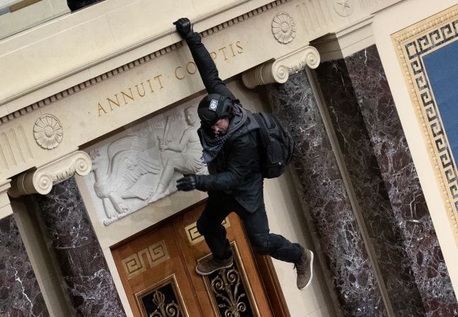 6 de enero — un hombre cuelga de un balcón en la cámara del Senado. Los agitadores también invadieron la oficina de la presidenta de la Cámara de Representantes, Nancy Pelosi. Fueron necesarias varias horas para asegurar el Capitolio. Los legisladores regresaron esa noche y reanudaron el recuento de votos.