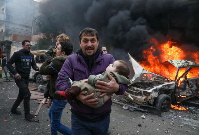31 de enero — un hombre lleva a una joven víctima de la explosión de un coche bomba en Azaz, Siria. El conflicto en curso en Siria comenzó después de un levantamiento en marzo de 2011 que se convirtió en una guerra civil. Desde entonces, cientos de miles han muerto y millones de personas han sido desplazadas por los combates en la región.