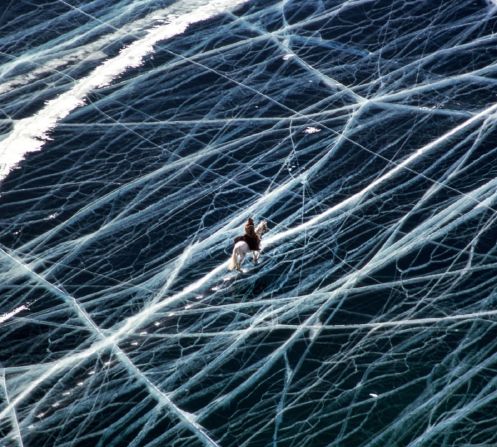 Matthieu Paley - Ice Rider Siberia. Una vista ddesde arriba del lago Baikal, el mayor lago de agua dulce del mundo. "Durante el invierno, el hielo tiene un grosor de hasta 1,5 metros, lo que permite a los camiones y a los animales cruzar con seguridad", explica el fotógrafo Matthieu Paley a Vital Impacts. "Las líneas blancas son grietas en el hielo y, cuando cambian las temperaturas, éstas emiten fuertes ruidos estremecedores, lo que refuerza la inquietante atmósfera". Crédito: Matthieu Paley