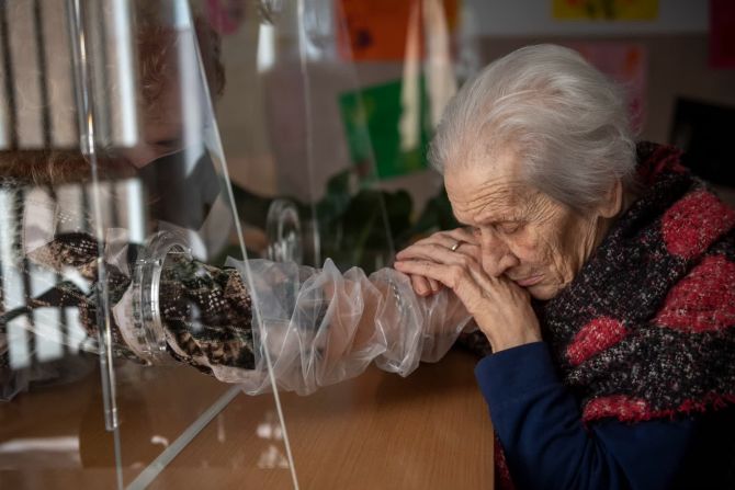 24 de febrero — Anna, residente del asilo de ancianos Villa Sacra Famiglia, toma la mano de su hija en la "sala de abrazos" de las instalaciones de Roma. La habitación permite que los residentes y sus familias se toquen entre sí mientras se mantienen a salvo del covid-19.