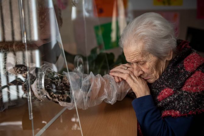 24 de febrero — Anna, residente del asilo de ancianos Villa Sacra Famiglia, toma la mano de su hija en la "sala de abrazos" de las instalaciones de Roma. La habitación permite que los residentes y sus familias se toquen entre sí mientras se mantienen a salvo del covid-19.