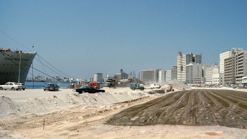 Esta fotografía de la carretera de Baniyas fue tomada en 1977. La carretera se está ampliando en terrenos recientemente ganados a las aguas de Dubai Creek. Al mirar más hacia el interior, se ve cómo la zona se ha desarrollado con torres de oficinas de reciente construcción. El edificio más alto de la fotografía era el más alto de Dubái hasta la construcción del World Trade Centre, según Reisz. Cortesía de Mark Harris, Biblioteca John R. Harris