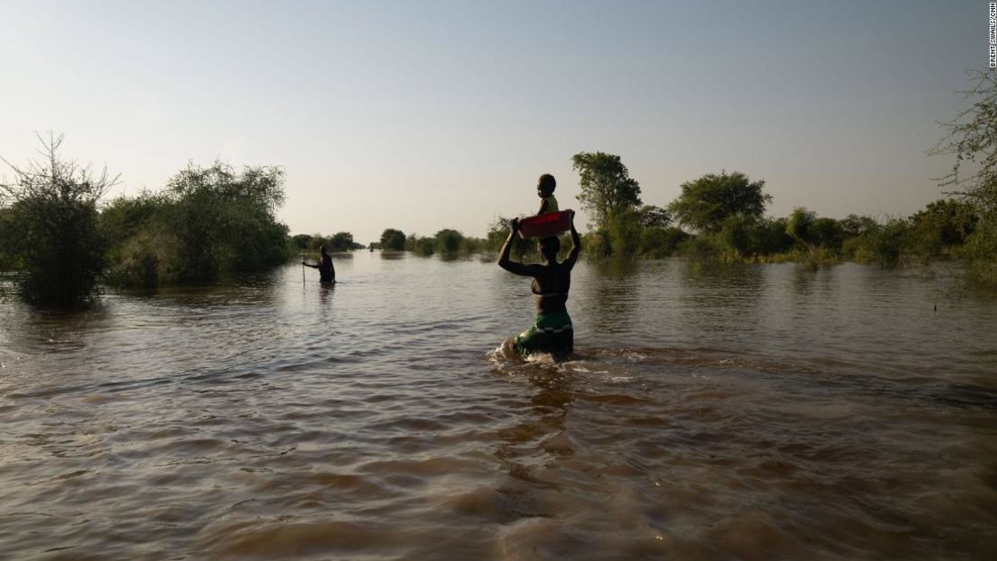 Una mujer lleva a su bebé en la cabeza mientras camina a través de las aguas de la inundación.