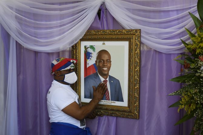 22 de julio — un hombre toca un retrato del fallecido presidente haitiano Jovenel Moise afuera de una catedral donde se llevó a cabo un servicio conmemorativo en Cap-Haitien, Haití. Moise fue asesinado en julio durante un ataque a su residencia privada.
