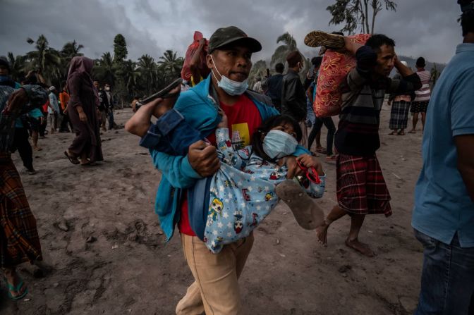 5 de diciembre – un hombre carga a un niño mientras otras personas rescatan sus pertenencias de un área cubierta de ceniza volcánica en la aldea de Sumberwuluh en el distrito de Lumajang en Indonesia. El monte Semeru hizo erupción un día antes y mató a decenas de personas.
