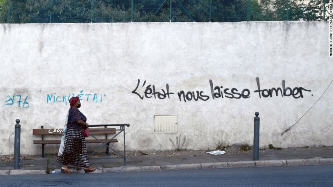 Una mujer pasa junto a un grafiti en una pared en el que se lee "El Estado nos defrauda" en una calle del barrio de Les Marronniers, en Marsella, en agosto de 2021.