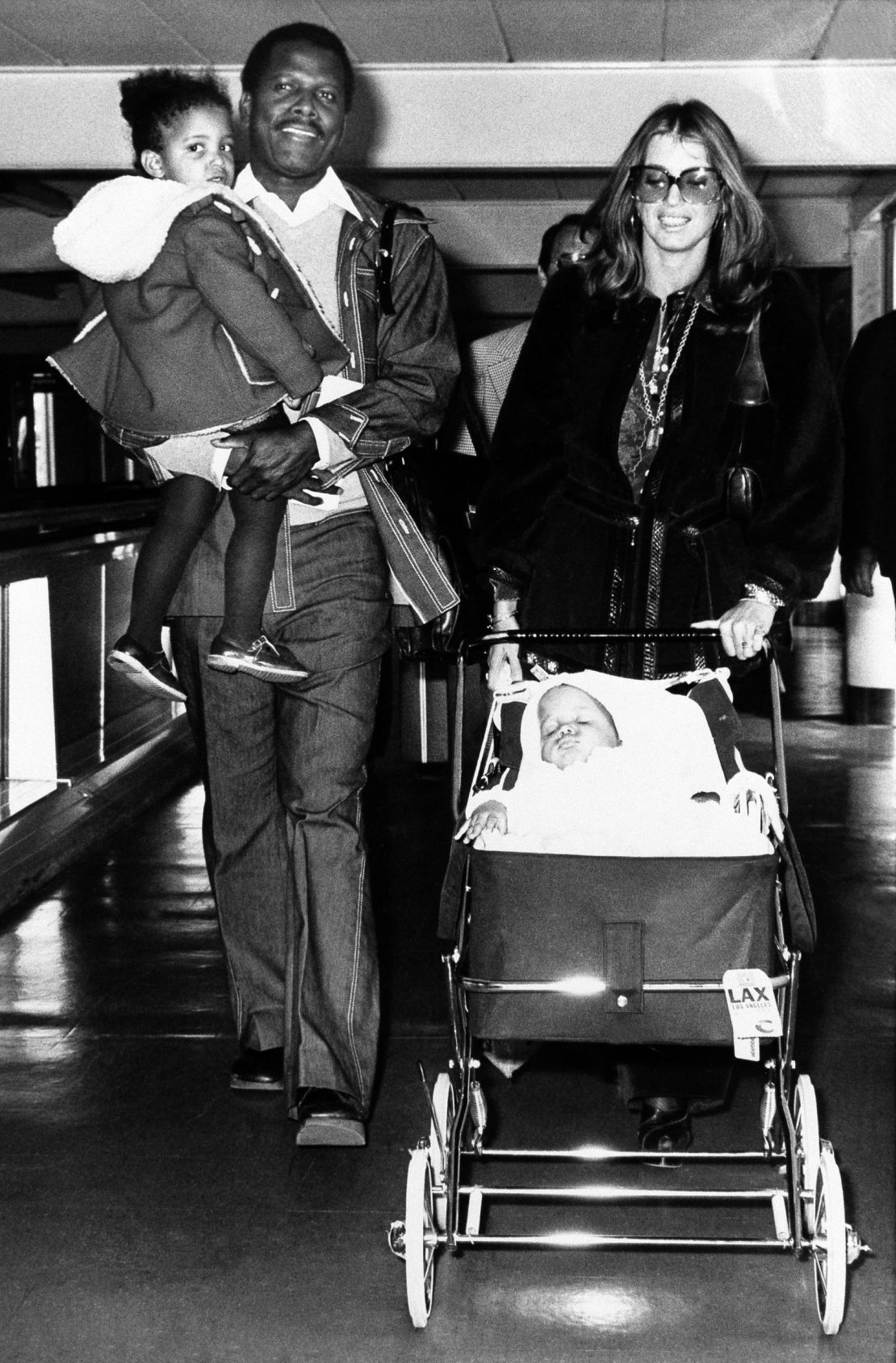 Poitier lleva a su hija Anika mientras su esposa, la actriz Joanna Shimkus, lleva a su hija menor Sydney en el aeropuerto de Heathrow en Londres en 1974. Crédito: Press Association/AP