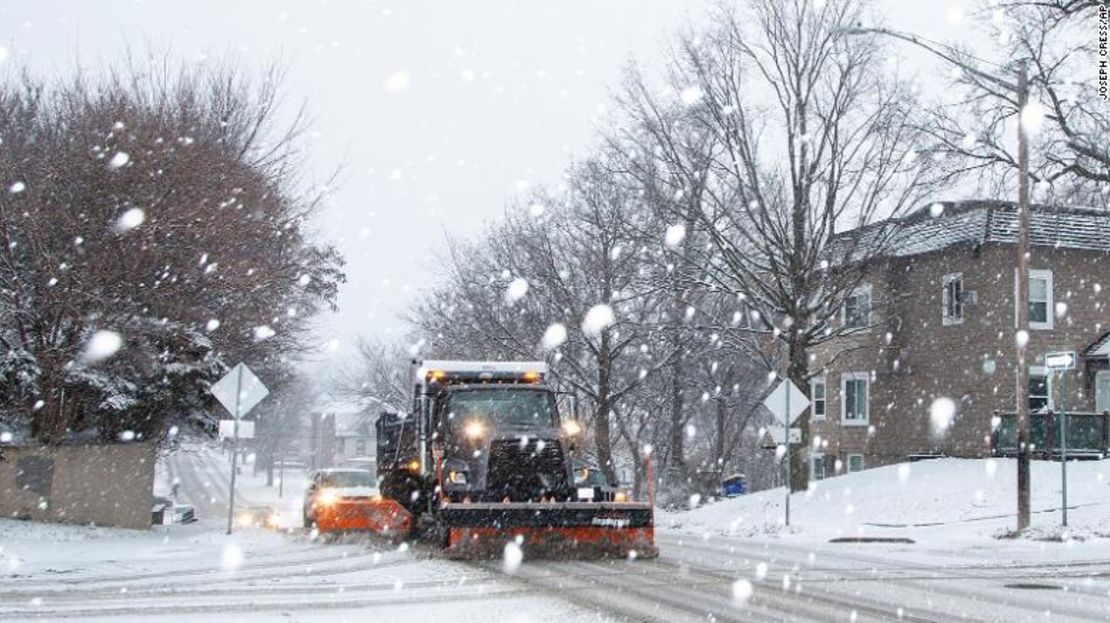Un conductor de una máquina quitanieves de Iowa City levanta aguanieve a lo largo de Dodge Street mientras la nieve cae durante una advertencia de tormenta invernal el 14 de enero de 2022, en Iowa City, Iowa.