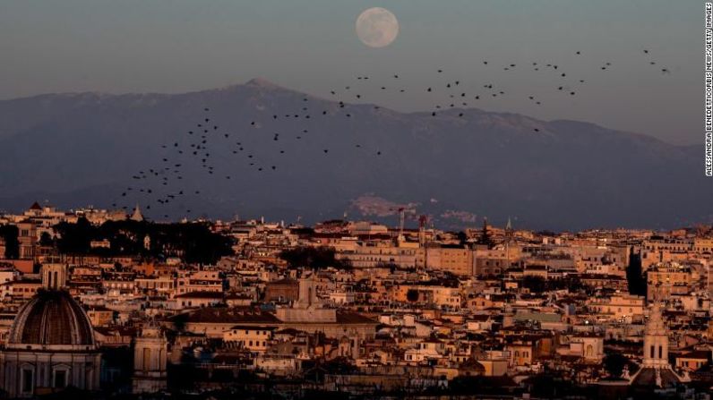 Estorninos vuelan en el cielo mientras la luna llena se eleva sobre la ciudad de Roma, Italia, el 17 de enero.