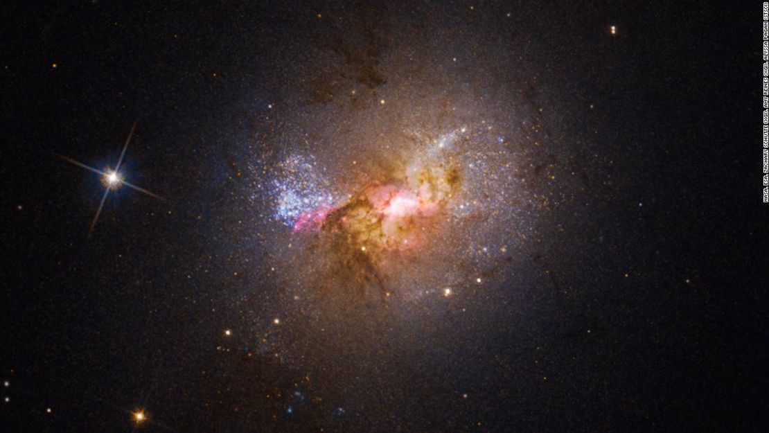 Esta imagen del telescopio espacial Hubble muestra la galaxia enana Henize 2-10, que está llena de estrellas jóvenes. El centro brillante, rodeado de nubes rosadas, indica la ubicación de su agujero negro y las áreas de nacimiento de estrellas.