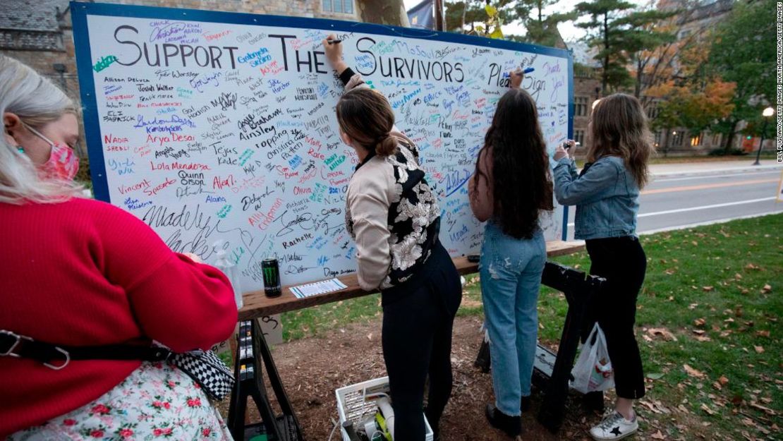 Los asistentes agregan sus firmas a un tablero en apoyo de los sobrevivientes de abuso sexual en una vigilia frente a la casa del presidente saliente de la Universidad de Michigan, Mark Schlissel, el 13 de octubre de 2021 en Ann Arbor, Michigan.