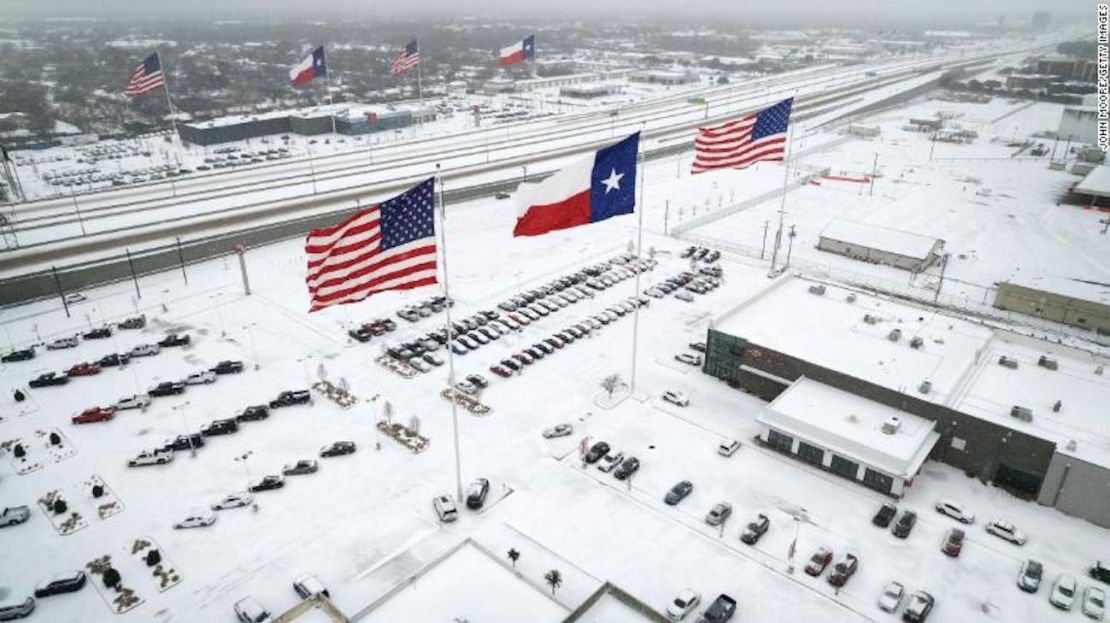 Las banderas ondean sobre los concesionarios de automóviles mientras el tráfico ligero se mueve a través de la nieve y el hielo en la Ruta 183 en Irving, Texas, el 3 de febrero.