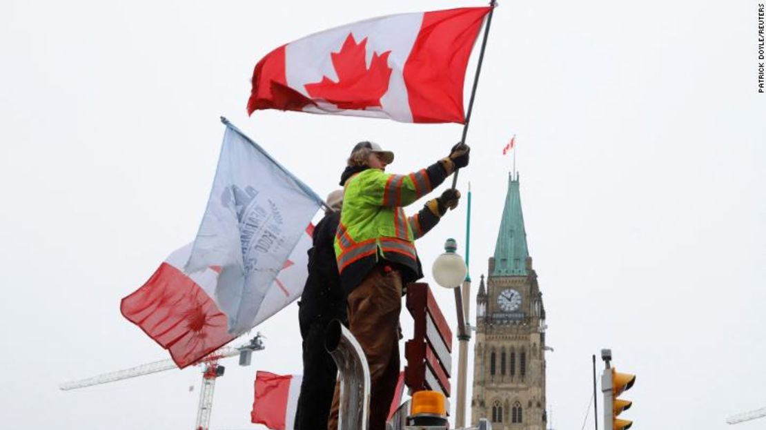 Personas ondean banderas en la parte superior de un camión frente al Parlamento este domingo, mientras los camioneros y sus seguidores continúan protestando por los mandatos de vacunación contra el covid-19 en Ottawa.