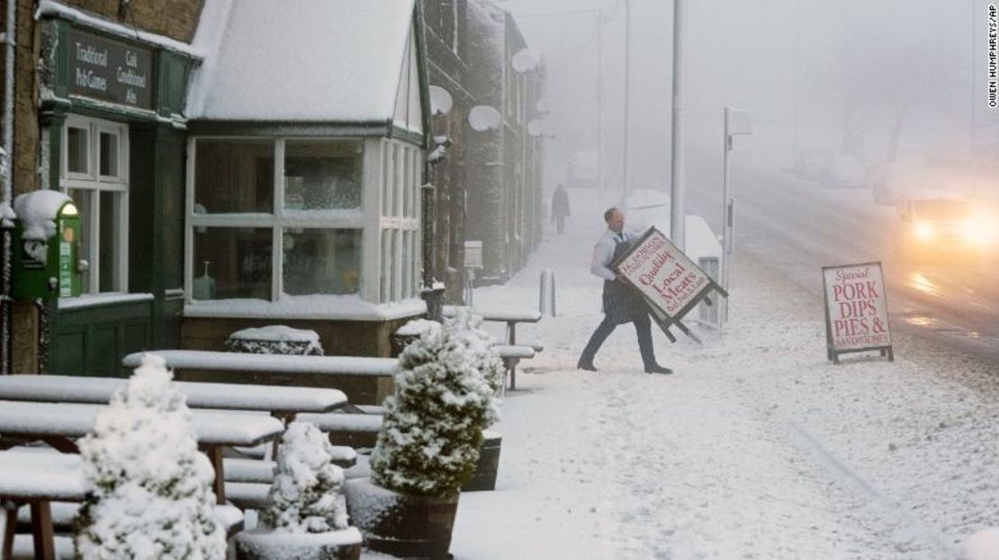 Un carnicero local carga el letrero de su tienda a través de un pavimento nevado en el condado de Durham, Gran Bretaña, luego de que la tormenta Eunice tocara tierra.