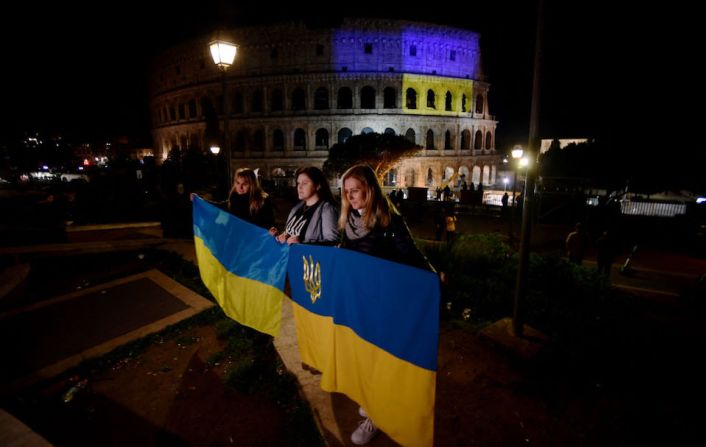 Manifestantes sostienen banderas ucranianas frente al Coliseo, iluminado con los colores de la bandera ucraniana, en Roma el 24 de febrero de 2022, después de la invasión rusa de Ucrania.