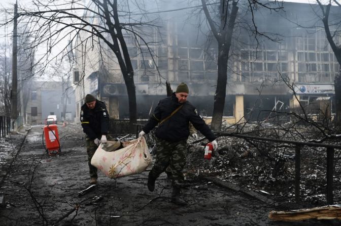 Agentes de policía retiran el cuerpo de un transeúnte que murió en el ataque aéreo que golpeó la principal torre de televisión de Kyiv el 2 de marzo de 2022. Atrás se ve la devastación de edificios cercanos tras el bombardeo.