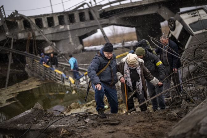 Un militar local ayuda a una anciana a cruzar un puente que fue sido destruido por la artillería en las afueras de Kyiv el 2 de marzo.