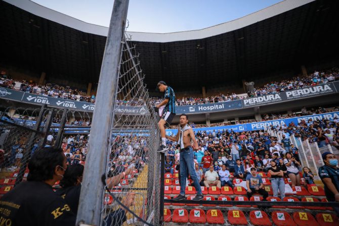 Los aficionados escalan la cerca de alambre para ingresar al campo durante el partido de la novena ronda entre el Querétaro y el Atlas.