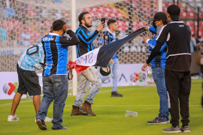 Los aficionados del Querétaro queman una bandera del Atlas mientras invaden la cancha durante el partido de novena ronda de la Liga MX en el estadio La Corregidora.