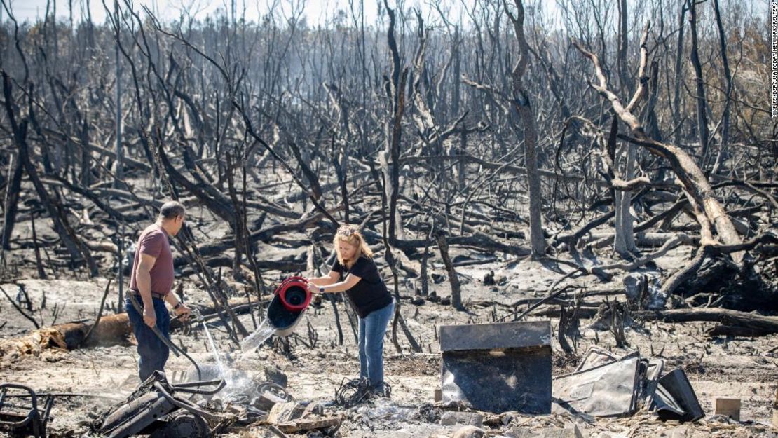 Héctor Rivera y Wandi Blanco vierten agua en puntos críticos sobre el cobertizo de un vecino junto a su casa el sábado, después de que el incendio Adkins arrasara el área en la ciudad de Panamá, Florida.