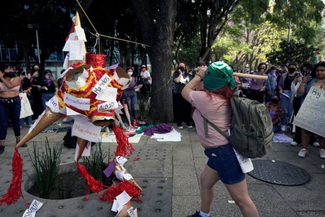 Una mujer rompe una piñata con letreros que dicen "acoso", "mansplaining" y "machismo" en la Ciudad de México.