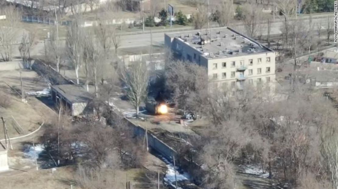 Esta captura de pantalla de las imágenes del dron muestra un vehículo militar disparando cerca de un edificio.