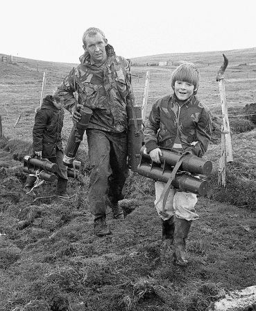 Stephen Dickson, de ocho años, ayuda a un soldado del Regimiento de Paracaidistas a transportar una bomba de mortero en esta fotografía tomada en mayo de 1982 en Puerto San Carlos, Islas Malvinas.