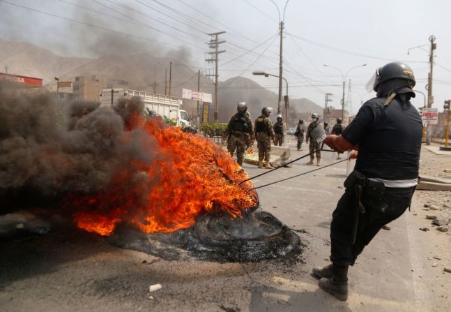 Un policía intenta extinguir una barricada incendiada durante el paro de transportistas al este de Lima que provocó bloqueos en varias carreteras de seis regiones de Perú.