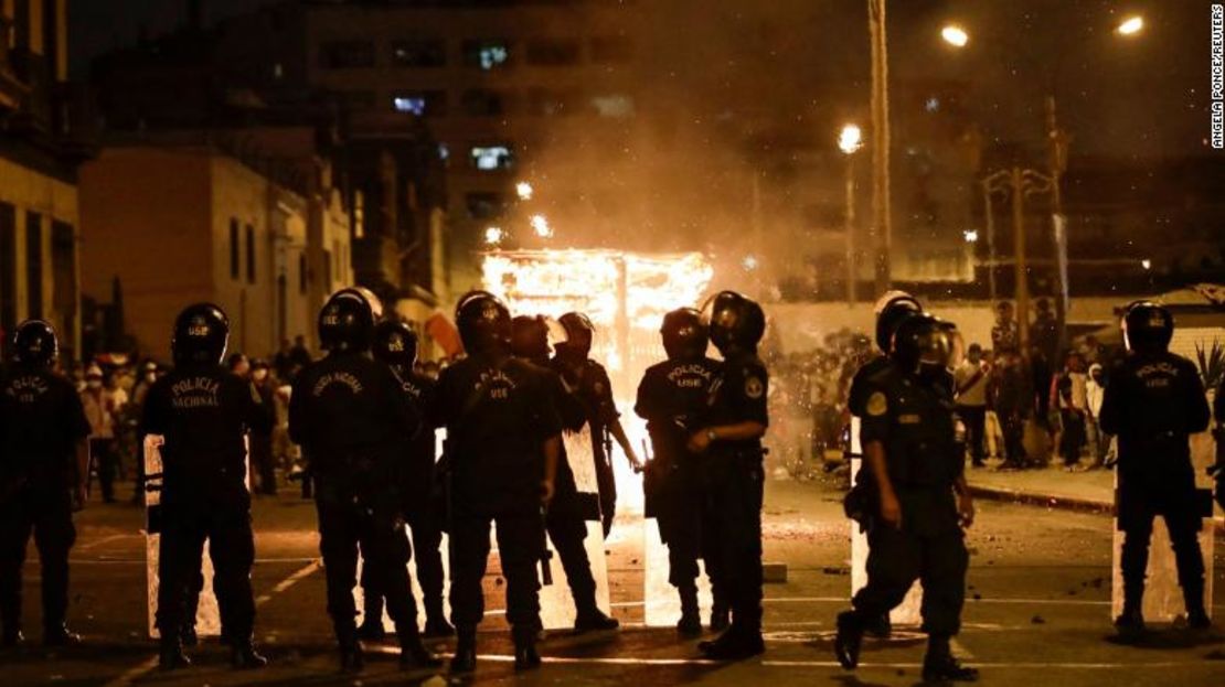 Agentes de policía en Lima se ubican frente a una estructura de vendedores ambulantes en llamas durante una manifestación contra el presidente Pedro Castillo. Las protestas comenzaron por el aumento de los precios del combustible y los fertilizantes, a raíz de la guerra de Rusia en Ucrania, pero su alcance se ha ampliado.