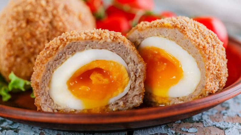 Huevos escoceses (Reino Unido): El huevo escocés, posiblemente el tentempié más proteico de la historia de la cocina, es un huevo duro envuelto en salchicha que se reboza en pan molido y se fríe hasta quedar crujiente. Crédito: koss13/Adobe Stock