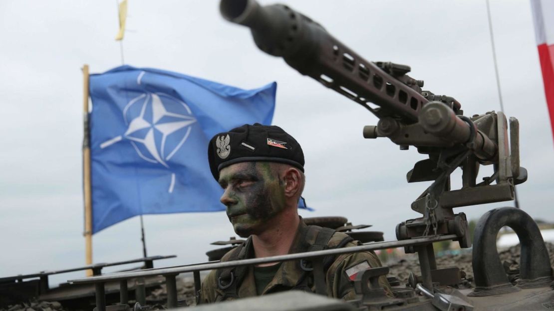 Un soldado polaco a bordo de un vehículo blindado, con la bandera de la OTAN.