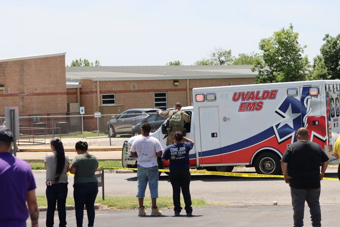 Una ambulancia está en el lugar mientras la gente observa detrás de la cinta policial. Pete Luna/Uvalde Líder-Noticias