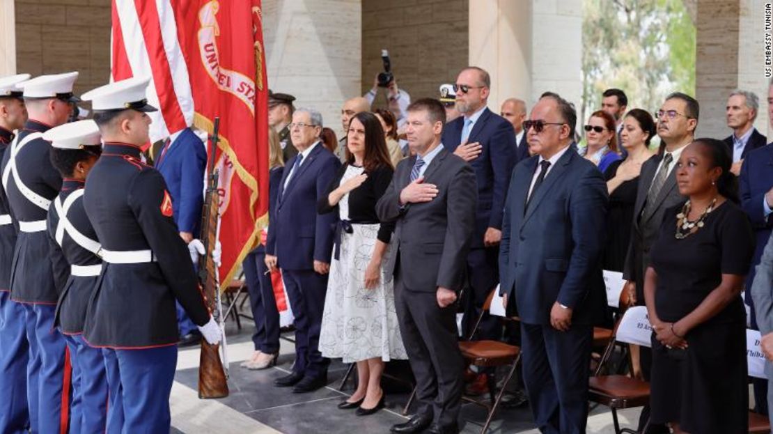 Asistentes de pie durante la ceremonia del Día de los Caídos en el Cementerio Norteamericano de África. El ministro de Relaciones Exteriores de Túnez, Othman Jerendei (primera fila, izquierda), junto a la diplomática de la embajada de Estados Unidos en Túnez, Natasha Franceschi.