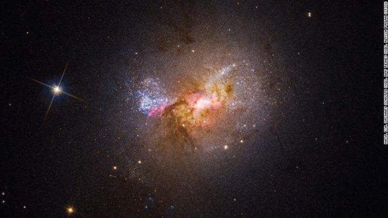 Esta imagen del telescopio espacial Hubble muestra la galaxia enana Henize 2-10, que está llena de estrellas jóvenes. El centro brillante, rodeado de nubes rosadas, indica la ubicación de su agujero negro y las áreas de nacimiento de estrellas.