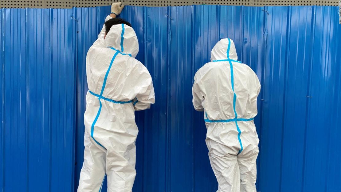 Trabajadores en trajes de materiales peligrosos instalan barreras fuera de un edificio en Shanghái el 9 de junio, para evitar que los residentes salgan.