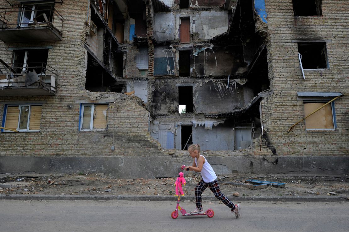 Una niña pasa con un patinete por delante de un edificio residencial destruido en el pueblo de Horenka, en la región de Kyiv, el 4 de junio de 2022, en medio de la invasión rusa de Ucrania.