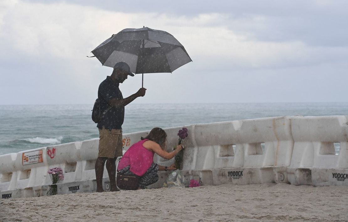 Eliagne Sanchez y K. Parker colocan flores en la playa cerca del edificio parcialmente colapsado.