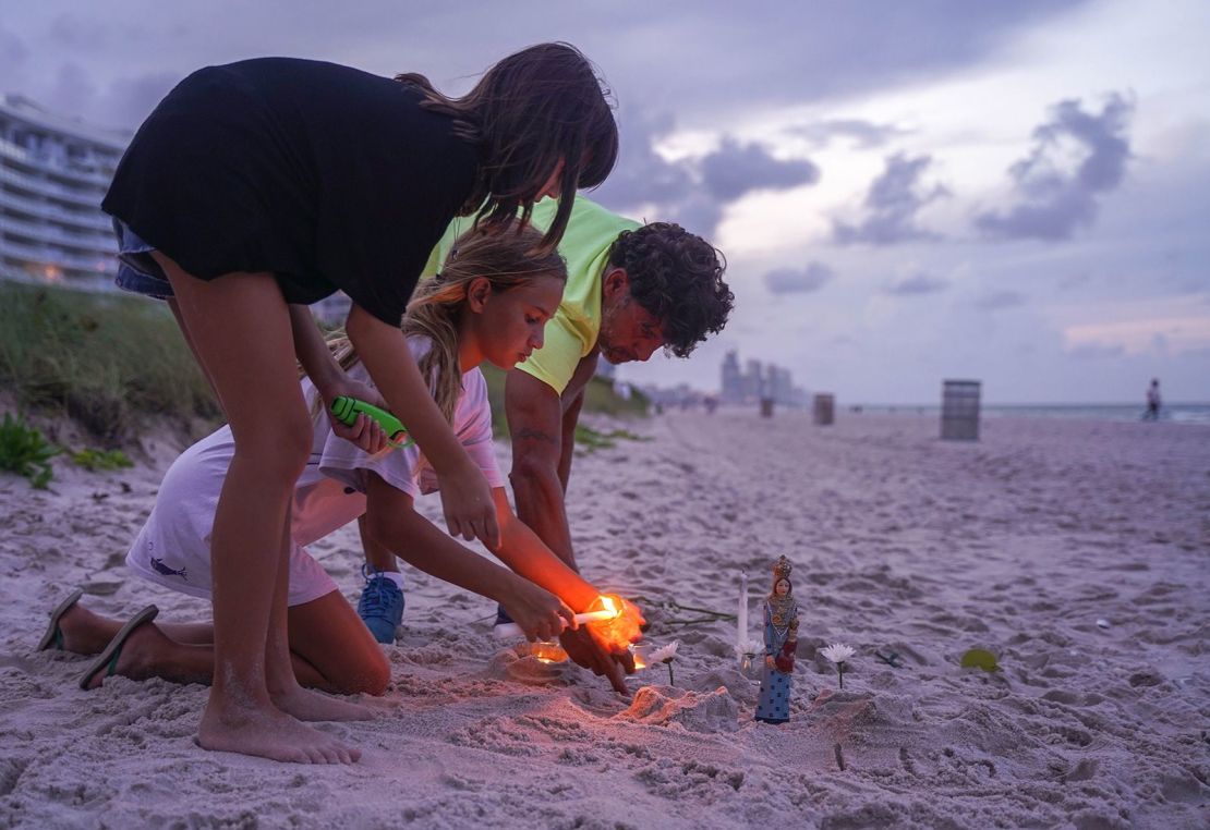 Personas en duelo encienden velas en la playa cerca del edificio.