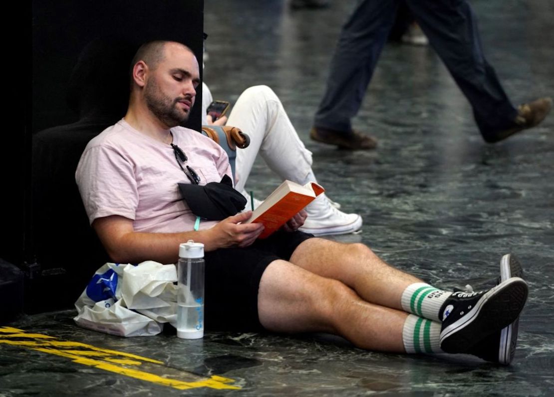 Un pasajero de tren se sienta con una botella de agua mientras lee un libro en la explanada de la estación de tren de Euston en el centro de Londres, el 19 de julio de 2022, cuando se cancelaron los servicios debido a un incendio en la vía y mientras el país experimenta una ola de calor extremo.