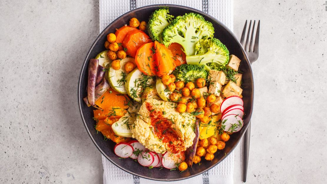 Una comida saludable a base de plantas incluye una colorida mezcla de verduras, garbanzos, hummus y tofu.