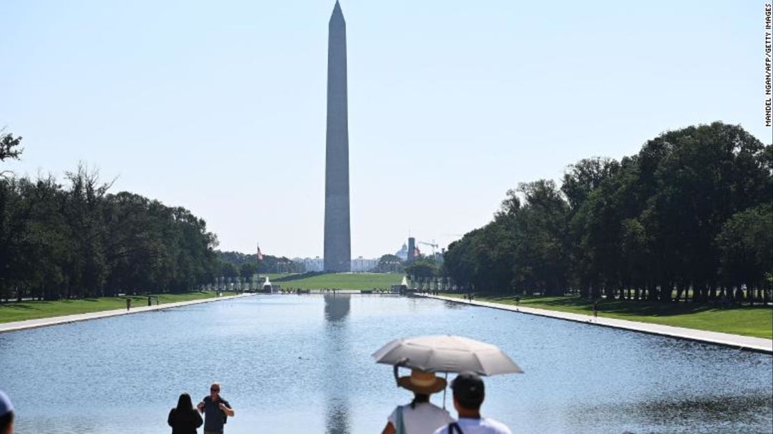 Las personas usan un paraguas para protegerse del sol mientras miran el Monumento a Washington en Washington, DC, este sábado.