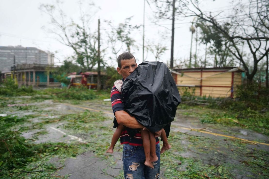 Un hombre lleva a sus hijos entre la lluvia y los escombros en Pinar del Río, el martes. Crédito: Alexandre Meneghini/Reuters