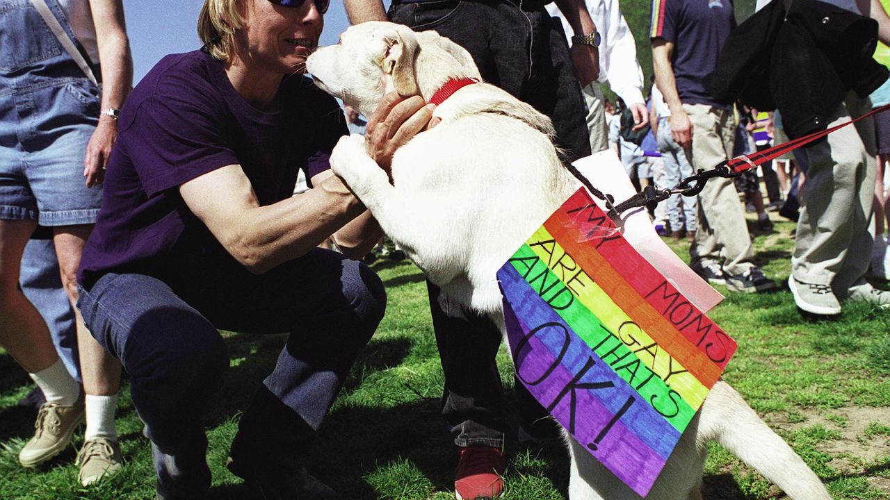WASHINGTON, : US tennis legend Martina Navratilova plays with a dog, who wears a sign with pro-Gay sentiments, during a Gay rights march 30 April 2000 in Washington, DC. Throngs of lesbian and homosexual protesters have converged on the US capital in a major show of force, combining political rallies, somber AIDS memorials and raucus celebrations. AFP PHOTO/Shawn THEW