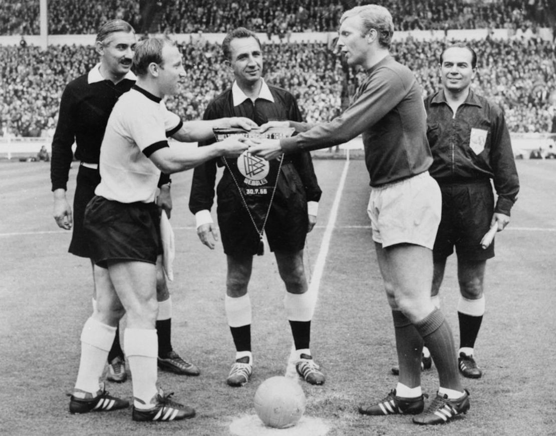 Los capitanes de los equipos nacionales de fútbol alemán e inglés, Uwe Seeler (izquierda) y Bobby Moore intercambian banderines mientras el árbitro suizo Gottfried Dienst (al centro) observa antes del comienzo de la final de la Copa del Mundo el 30 de julio de 1966 en el estadio de Wembley en Londres. FOTO DE AFP